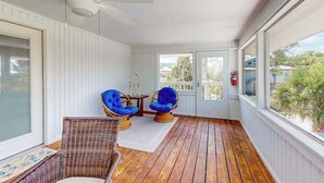 Un portico coperto con pavimento in legno, poltrone in vimini, una ventola a soffitto e ampie finestre.