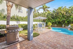 Um pátio com churrasqueira, móveis de exterior e piscina.