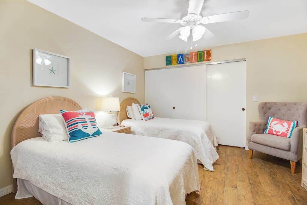 A hotel room with two beds, a ceiling fan, a wardrobe, and a chair.