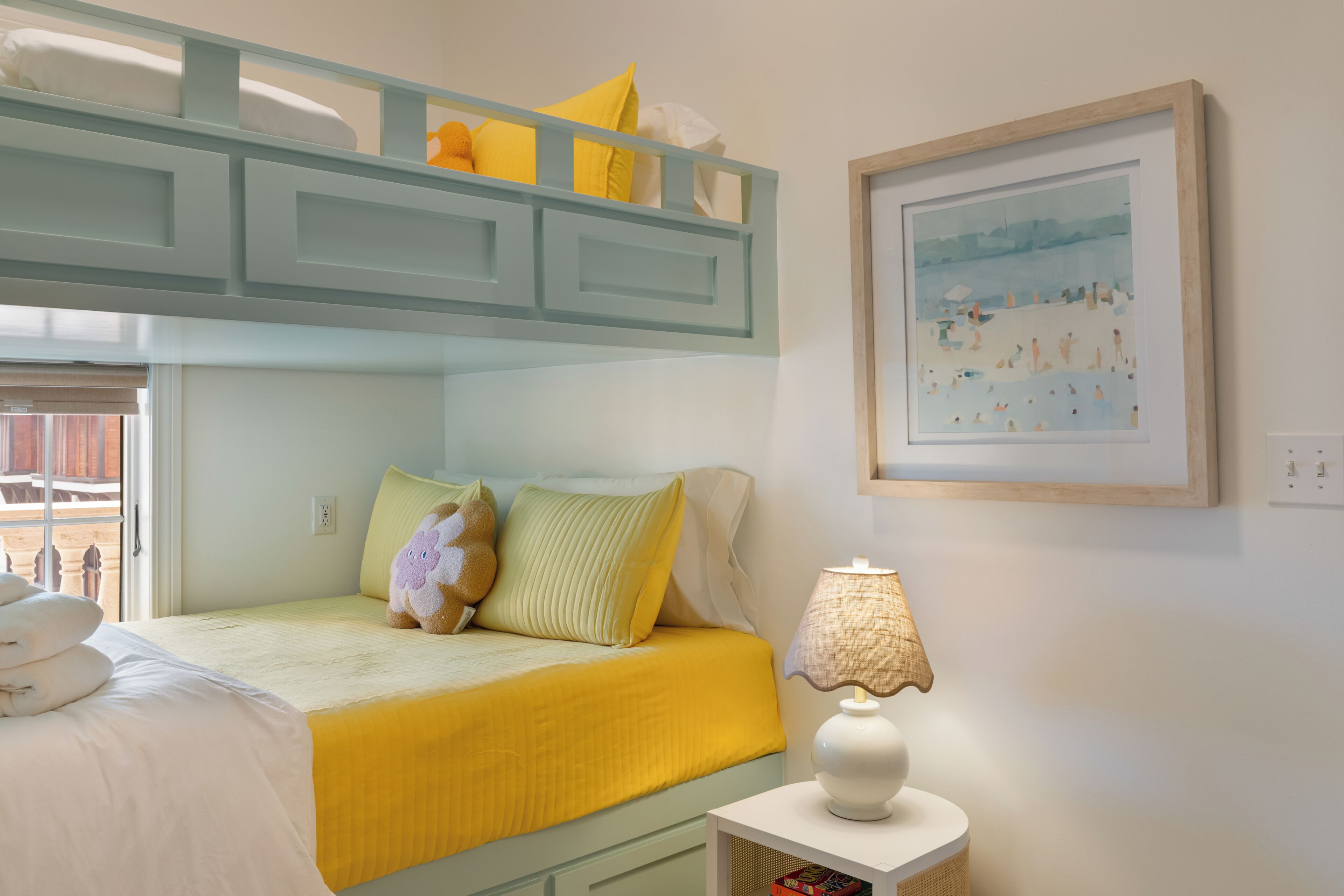 A bunk bed with a yellow bedspread, a lamp on a bedside table, and a framed picture on the wall.