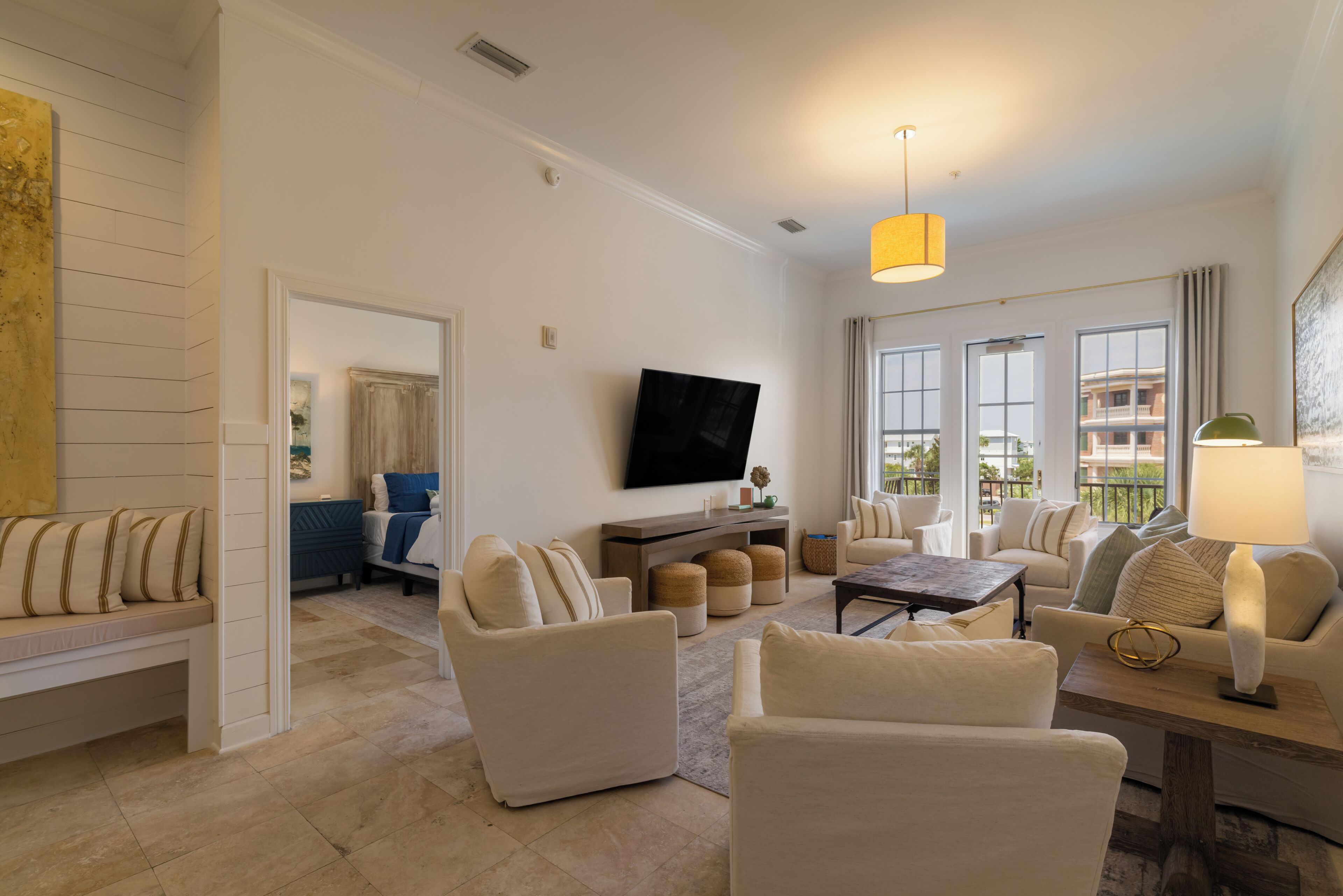 A modern living room with a flat-screen TV, comfortable seating, and large windows.