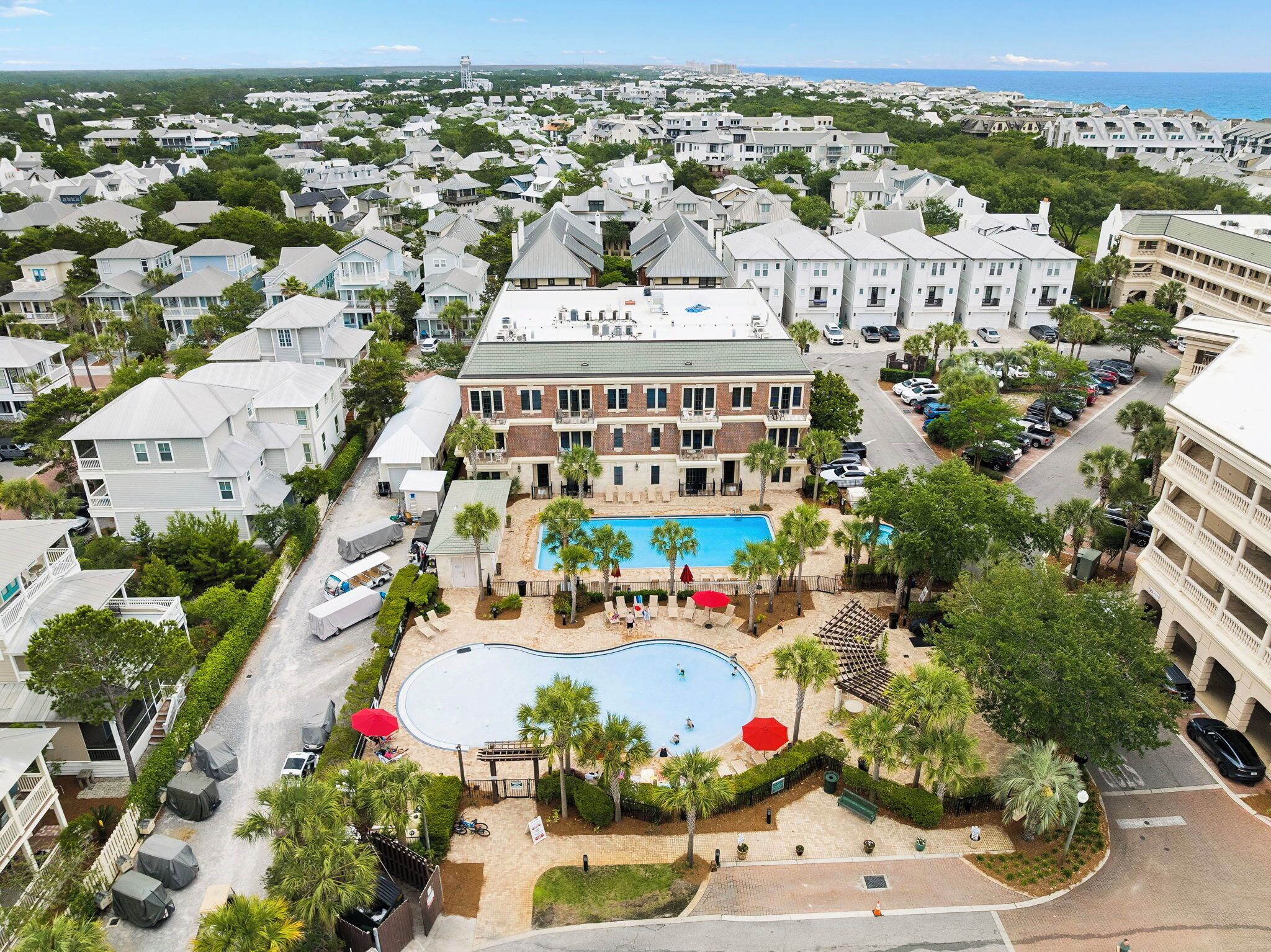 A large building with a swimming pool surrounded by palm trees and covered parking.