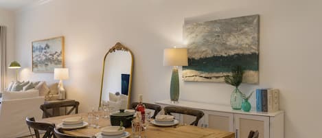 A dining area with a wooden table set for four, surrounded by chairs. A large mirror and a painting are on the wall.