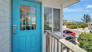 Een turquoise deur, een balkon met een hekwerk en een uitzicht op geparkeerde auto's en een gebouw op de achtergrond.