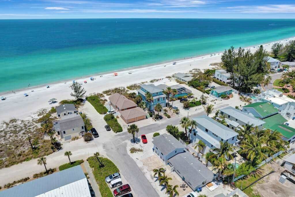 An aerial view of a coastal area with a beach, several buildings, and a clear view of the ocean.