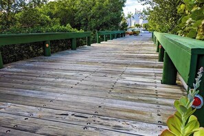 A wooden boardwalk with green railings, surrounded by lush greenery. - Inviting Condo with Shared Pool, High-Speed WiFi, and Central AC (Holmes Beach)