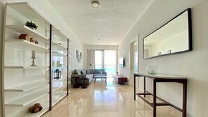 Amplia sala de estar con sofá, mesa de centro y un ventanal grande. Se observan estantes con objetos decorativos y un espejo en la pared.