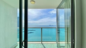 Un balcón con puerta de cristal que da a una piscina, con vistas al océano y montañas distantes.