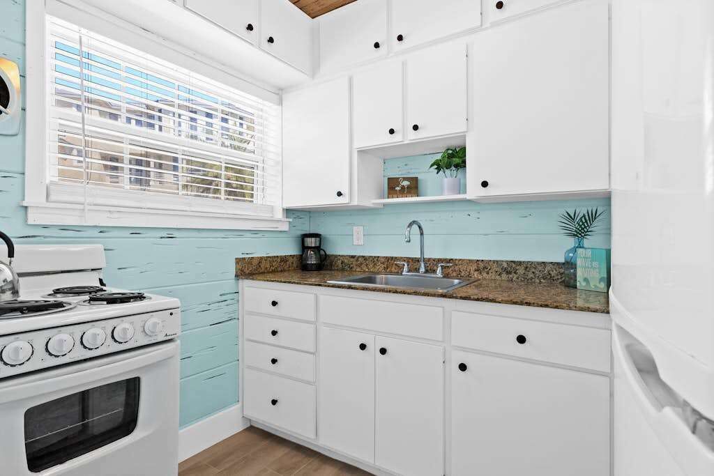 A kitchen with white cabinets, a stove, a sink, and a window with blinds.