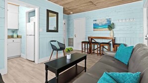 A room with a wooden ceiling, a light blue wall, a dining area with a table and chairs, a sofa with teal cushions, and a kitchen with white cabinets. - Charming Suite w Shared Pool, High-Speed WiFi - Steps to the Beach (Siesta Key)