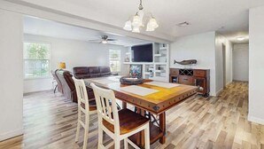A spacious living area with a wooden dining table, white chairs, a sofa, and a television. - Charming home w large yard, near Beaches, Sarasota, Bradenton, & the airport (Sarasota)