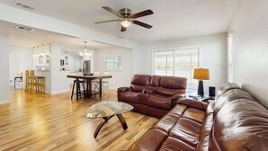 A spacious living room with a leather sofa, a glass coffee table, and a dining area with a table and chairs. - Charming home w large yard, near Beaches, Sarasota, Bradenton, & the airport (Sarasota)