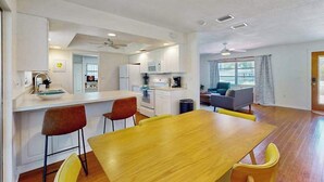 Une cuisine moderne avec des meubles blancs, un coin repas avec une table et des chaises en bois, et un salon avec un canapé et une table basse.