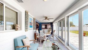Ein sonnendurchfluteter Raum mit Deckenventilator, einer Couch, einem Couchtisch und einem Essbereich mit Stühlen.