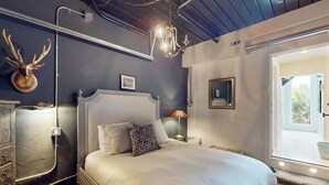 A bedroom with a large bed, a chandelier, a mounted deer head, and a window with a view. - Luxe bay-view escape with private pool, kayak, grill, ice box, & all-new interior (Sarasota)