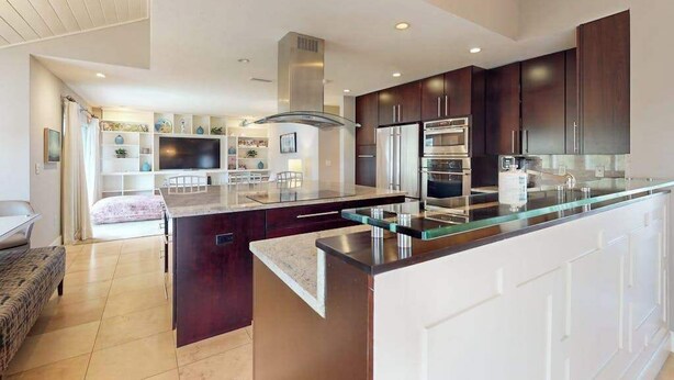 A modern kitchen with dark wood cabinets, stainless steel appliances, and a glass island. - Luxe bay-view escape with private pool, kayak, grill, ice box, & all-new interior (Sarasota)