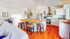 A modern kitchen with a central island, white cabinetry, and a dining area with a sofa and bar stools. - Canal-front home near Shell Beach with access to bay & deck (Sarasota)