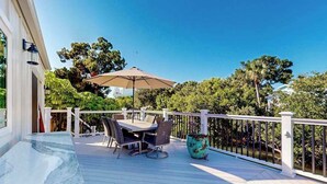 A wooden deck with outdoor furniture, a potted plant, and a view of trees and a building. - Canal-front home near Shell Beach with access to bay & deck (Sarasota)