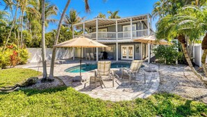 Une maison à deux étages avec une piscine, du mobilier d’extérieur et des palmiers.
