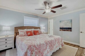 A bedroom with a bed, nightstands, a ceiling fan, a window with blinds, a door, and a painting on the wall. - Relaxing Home with Private Pool, High-Speed WiFi, Central AC, & Washer-Dryer (Anna Maria)