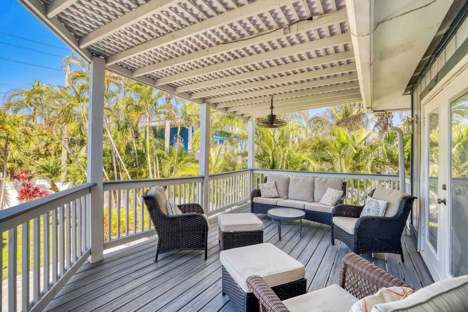 A covered outdoor seating area with wicker furniture and a view of tropical vegetation.