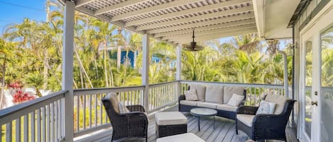 A covered outdoor seating area with wicker furniture and a view of tropical vegetation.