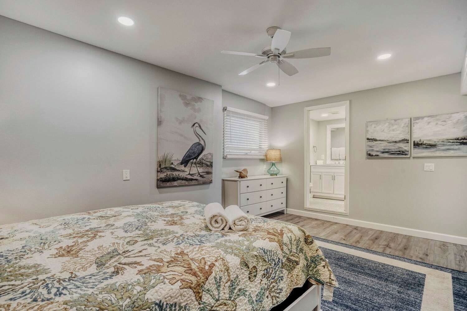 A bedroom with a bed, a ceiling fan, a dresser, and artwork on the walls.