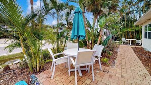 Une terrasse avec des chaises blanches et une table, entourée de palmiers et bordée d’un chemin en briques.