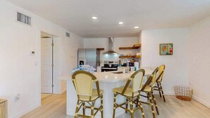 Une cuisine moderne dotée d’un îlot central, de meubles blancs et d’un coin repas avec des chaises en osier.