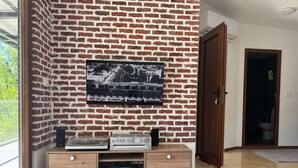 A room with a brick wall, a mounted television, a wooden cabinet, and a round table with snacks.
