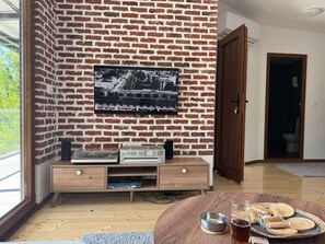 Una habitación con pared de ladrillo, televisor montado, mueble de madera y una mesa redonda con aperitivos.