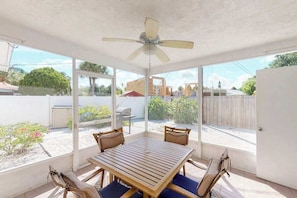 A covered patio with a table and chairs, a ceiling fan, and large windows offering a view of the backyard. - Comfortable island villa with private heated pool, courtyard & easy beach access (Holmes Beach)