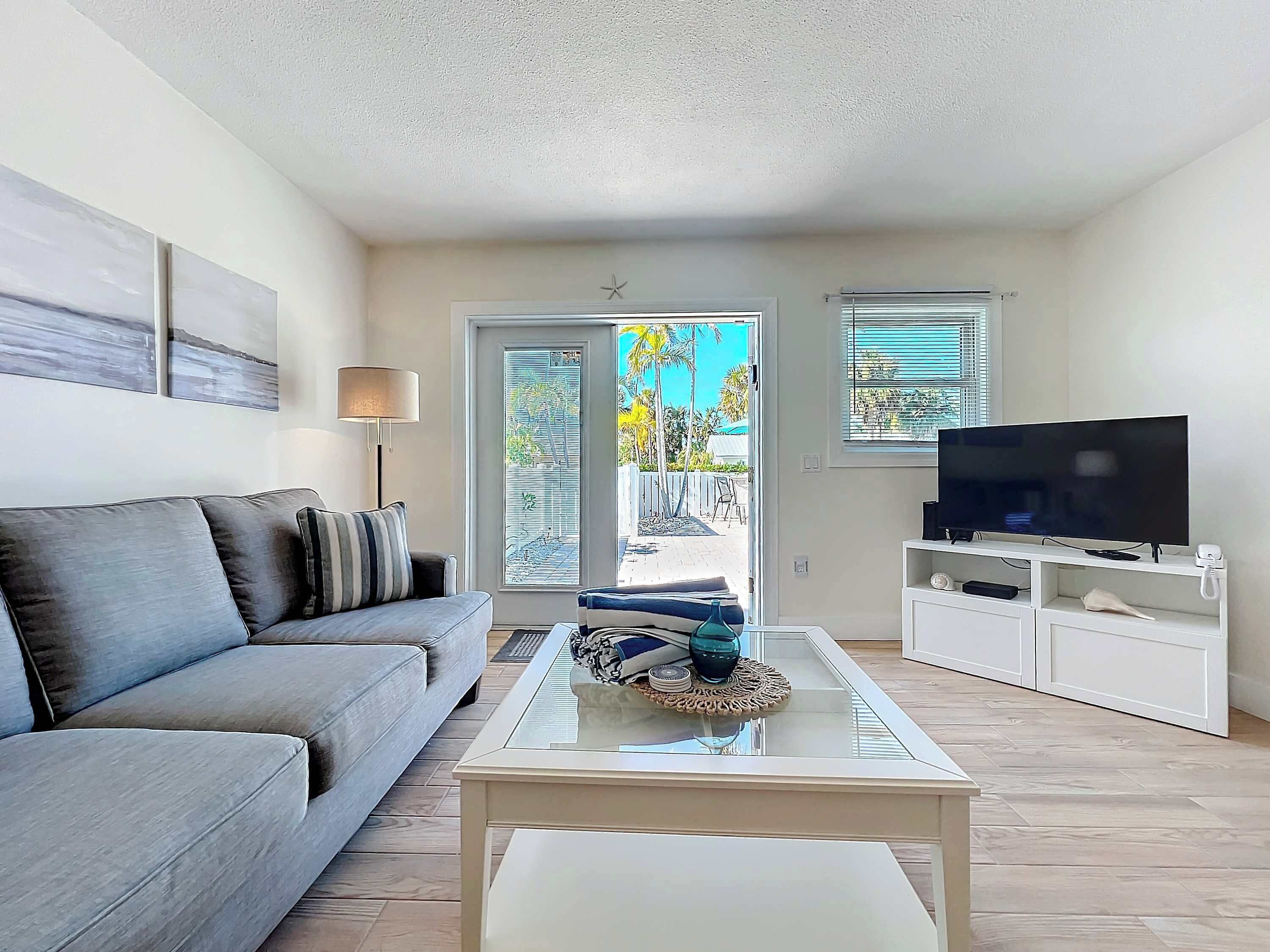 A living room with a sofa, a glass coffee table, a television, and a sliding glass door leading to an outdoor area.