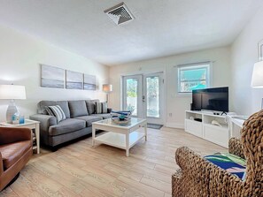 Ein Wohnzimmer mit Sofa, Couchtisch, Fernseher und Korbstuhl.