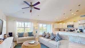 Uma sala de estar moderna com sofá, puf e ventilador de teto.