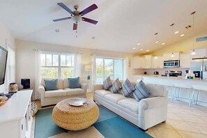 A modern living room with a sofa, ottoman, and a ceiling fan. - Beautiful lakeside home w upscale amenities, heated private pool & fishing dock (Holmes Beach)