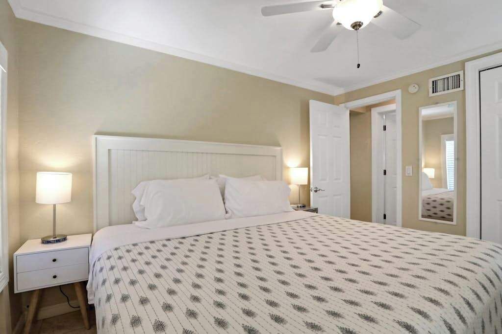 Une chambre à coucher avec un lit, des tables de chevet, un ventilateur de plafond et une porte.