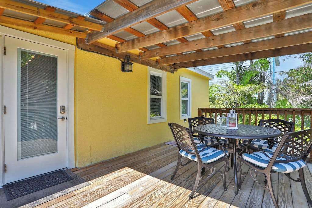Une terrasse couverte avec une plateforme en bois, une table ronde entourée de chaises et un mur jaune.