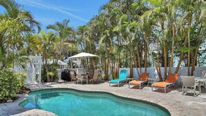 A swimming pool with lounge chairs and a covered seating area surrounded by palm trees. - Walk-up suite with on-site pool, private deck, full kitchen - walk to beach (Bradenton Beach)