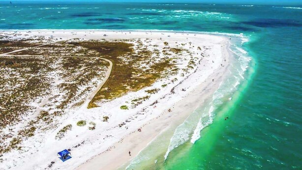 An aerial view of a beach with clear turquoise waters, a sandy shore, and sparse vegetation. - 2nd-floor duplex near beach with heated pool, balcony, grill, WD (Bradenton Beach)