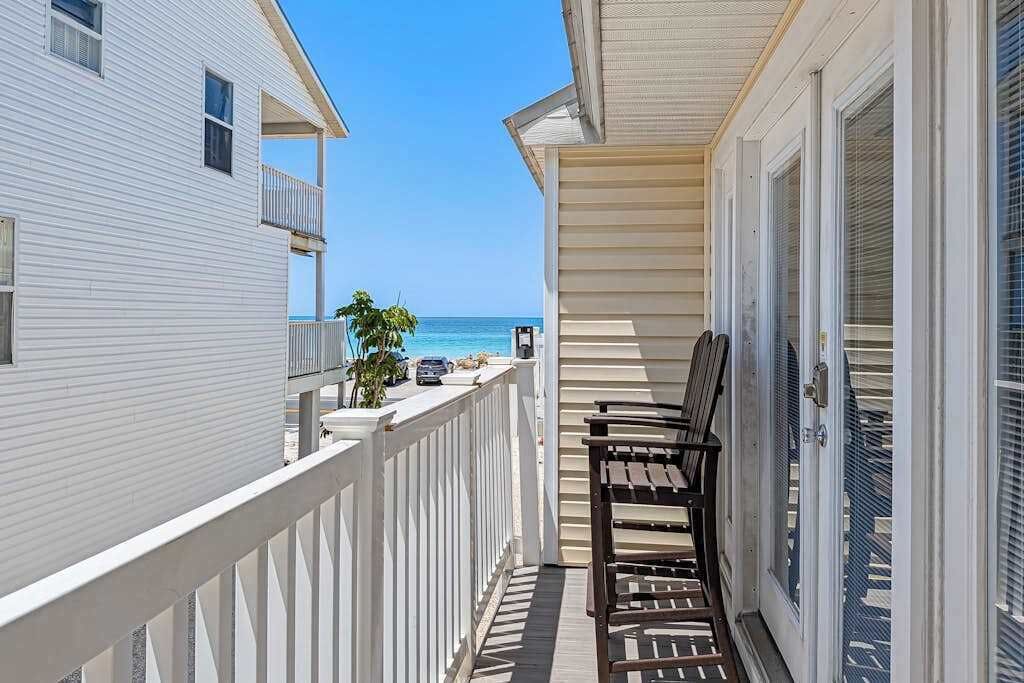A balcony with a view of the ocean, a wooden bench, and a white railing.