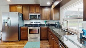 A kitchen with wooden cabinets, stainless steel appliances, a granite countertop, and a window. - Cozy home with private pool, lanai,  washer & dryer - minutes to beaches (Bradenton)