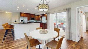 A modern kitchen with wooden cabinets, a central island, and a dining area with a round table and chairs. - Cozy home with private pool, lanai,  washer & dryer - minutes to beaches (Bradenton)