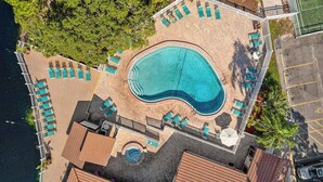 Vista aerea di un resort con piscina centrale, lettini prendisole e campo da tennis.