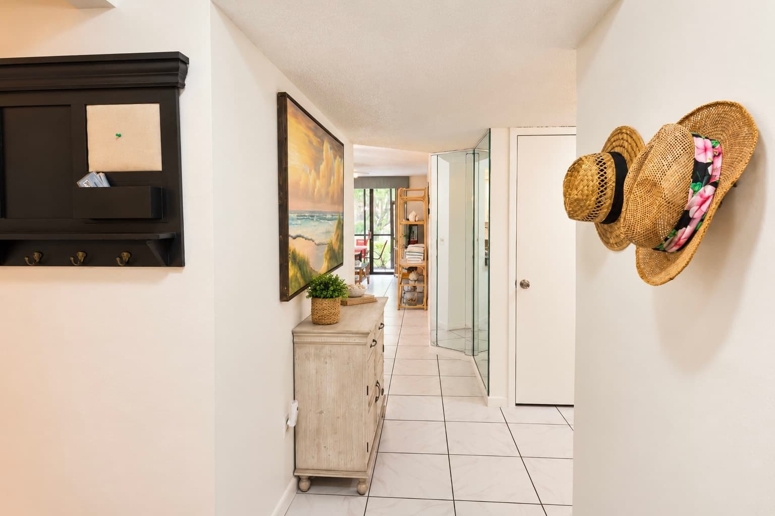 A hallway with a wooden cabinet, a painting, and a wicker hat on the wall.