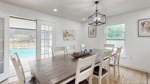 A dining area with a wooden table, white chairs, a chandelier, and artwork on the walls. - Spacious private home with  heating optional pool, patio, and large yard (Bradenton)