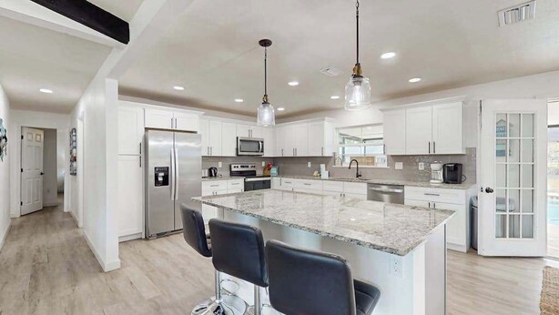 A modern kitchen with white cabinets, a central island with bar stools, stainless steel appliances, and pendant lighting. - Spacious private home with  heating optional pool, patio, and large yard (Bradenton)
