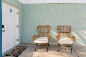Two wicker chairs with cushions against a textured wall, a white door with a number plate, and a welcome mat. - Boho Townhome Near Beach | Bikes & Beach Gear Included | Free Parking | W/D (Bradenton)