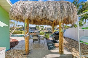 A thatched outdoor seating area with a pool and palm trees in the background. - Canal front home with boat access and and private pool and spa with fountain (Bradenton)