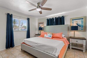 A bedroom with a bed, a ceiling fan, a window with curtains, a nightstand with a lamp, and a painting on the wall. - Canal front home with boat access and and private pool and spa with fountain (Bradenton)